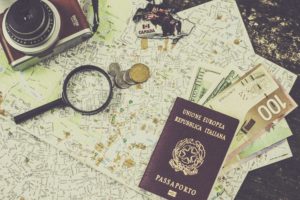 Samengesteld beeld met een landkaart, fototoestel, vergrootglas, munten, briefgeld en een paspoort. Photo by Francesca Tirico on Unsplash