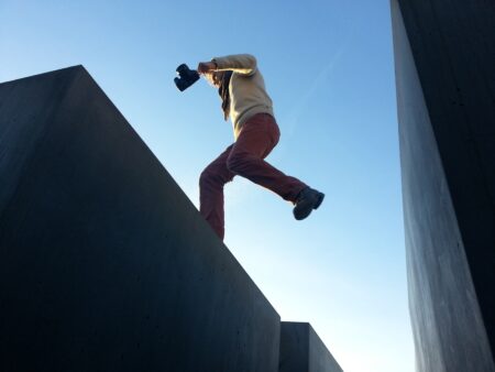 Man springt over een kloof tussen twee gebouwen, laagperspectief; foto van Sonja Guina via Unsplash